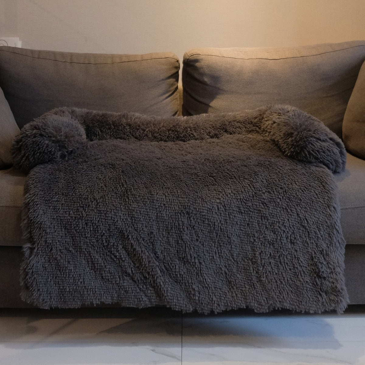 Dark grey plush dog bed with a raised edge on three sides, on a grey couch
