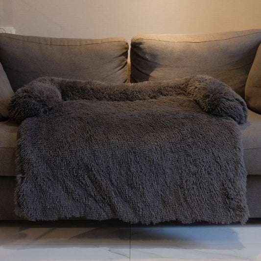 Dark grey plush dog bed with a raised edge on three sides, on a grey couch